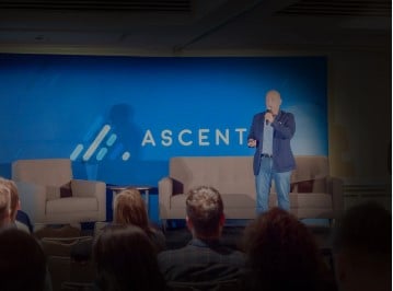 A speaker presenting on stage at the Ascent Conference in front of an attentive audience